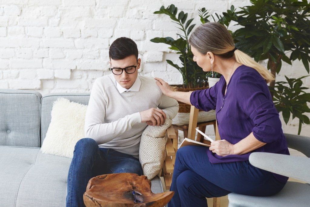 candid shot casually dressed professional woman psychotherapist her fifties touching her young male patient by shoulder while having counseling session expressing sympathy support ADD/ADHD
